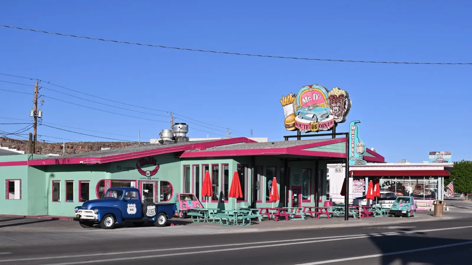 Pink and turquoise Mr. D'z Route 66 Diner in Kingman, Arizona, with a vintage blue pickup and picnic tables out front