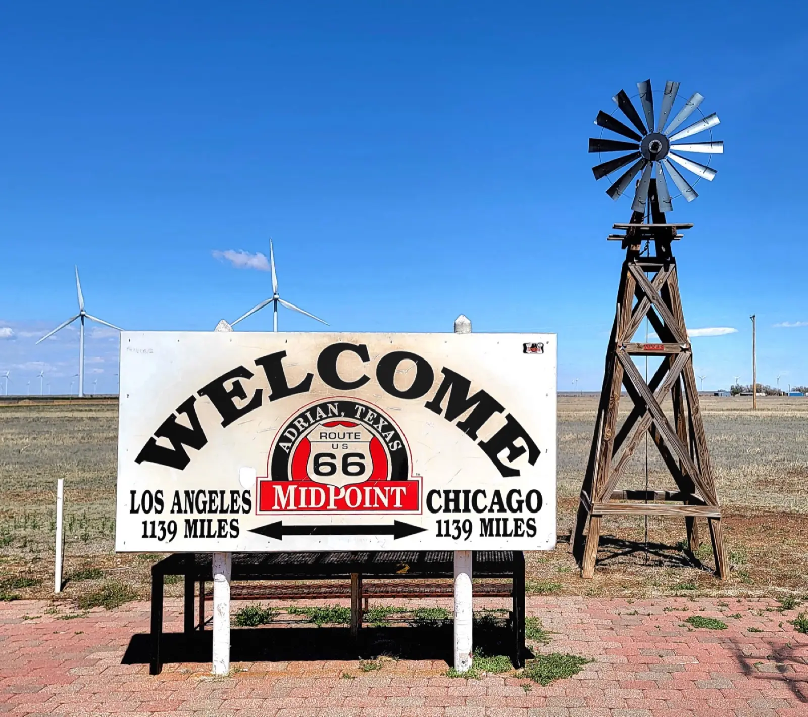 Welcome sign at the Midpoint Cafe in Adrian, Texas, showing 1,139 miles to Los Angeles and 1,139 miles to Chicago, beside a windmill