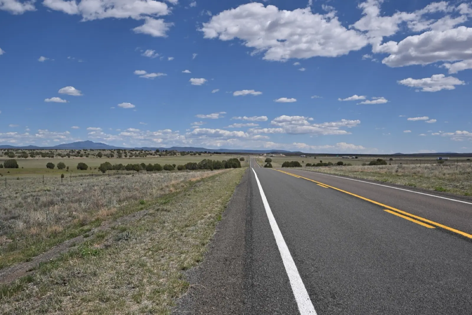 Two-lane Historic Route 66 near Crookton Road, Arizona, running straight across grassland under a blue sky with white clouds