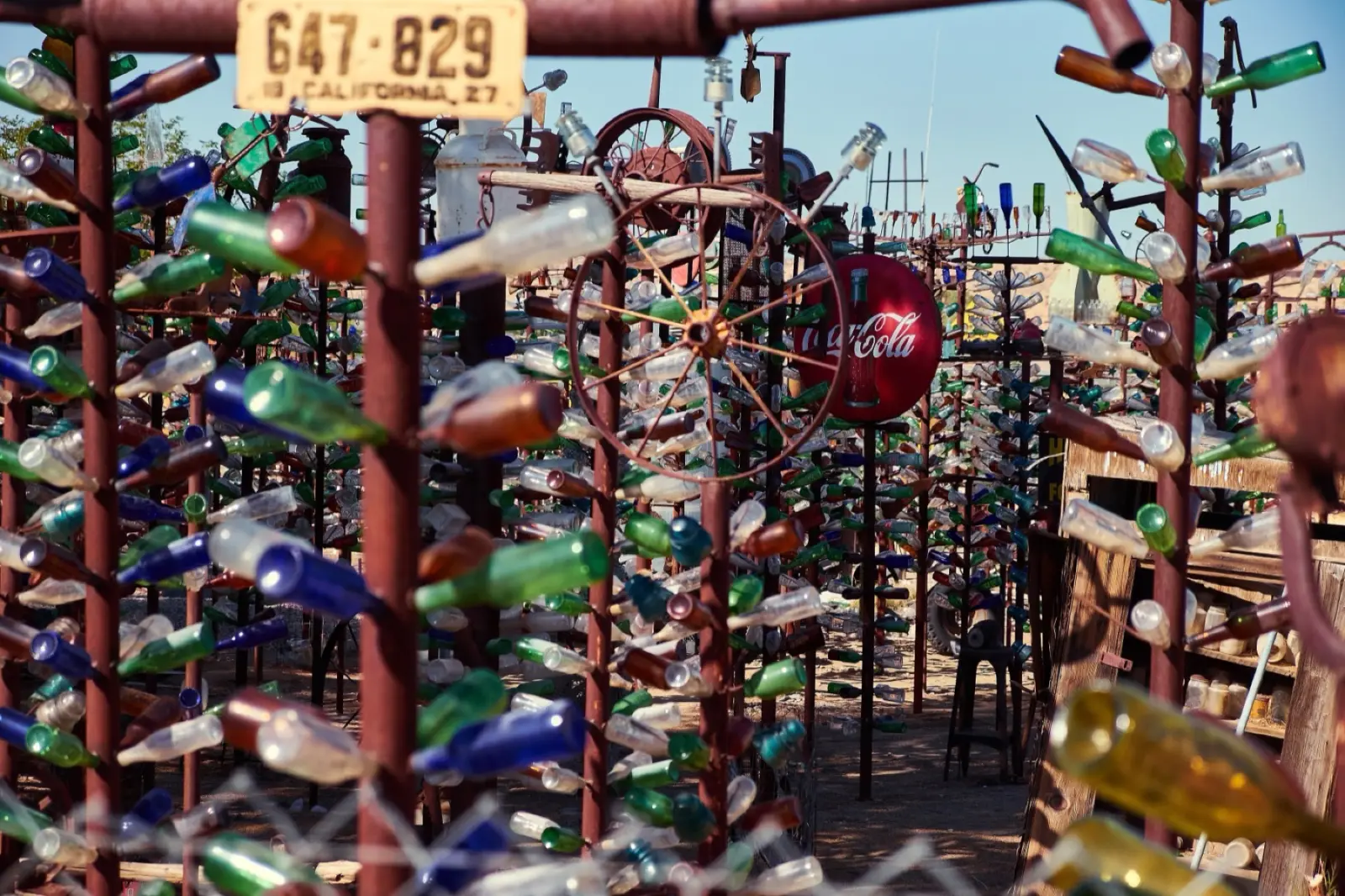 Metal poles hung with green, blue and clear glass bottles, an old license plate and a Coca-Cola sign at Elmer's Bottle Tree Ranch in Oro Grande, California
