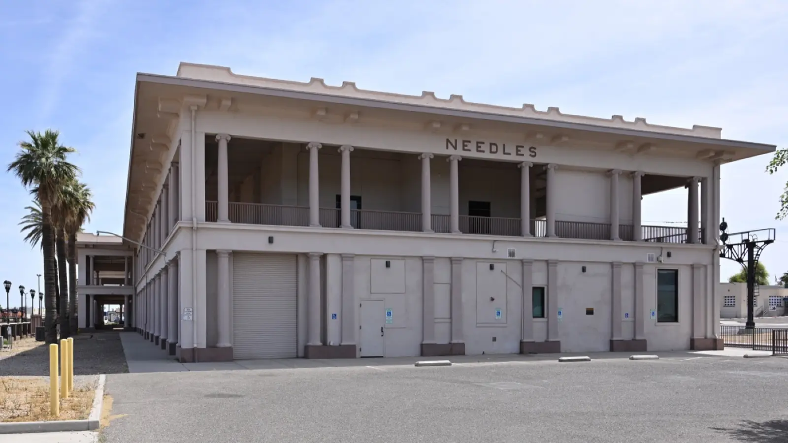 The restored El Garces Harvey House depot in Needles, California, a two-story white building with a colonnaded upper porch and NEEDLES in raised letters