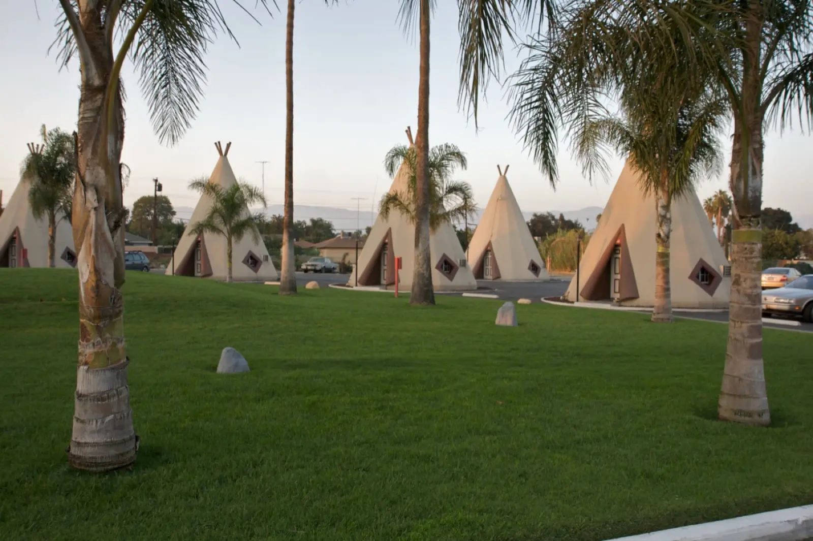 Cream-colored concrete teepees with dark trim among palm trees on a green lawn at the Wigwam Motel on Foothill Boulevard in San Bernardino, California