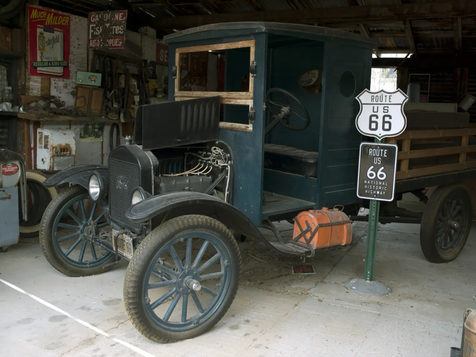 A restored Ford Model T truck beside a Route US 66 shield inside the garage at the Hackberry General Store, Arizona, with old signs on the walls