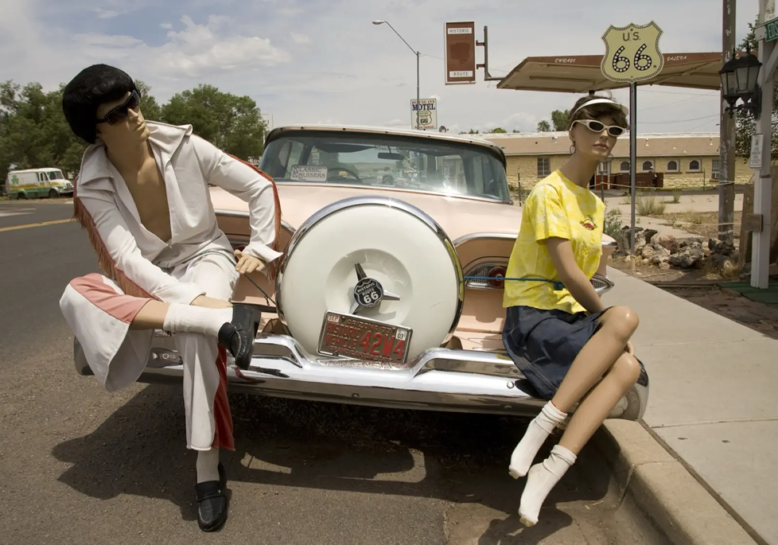 Mannequins posed beside a pink classic car under a Route 66 shield outside a souvenir store in Seligman, Arizona
