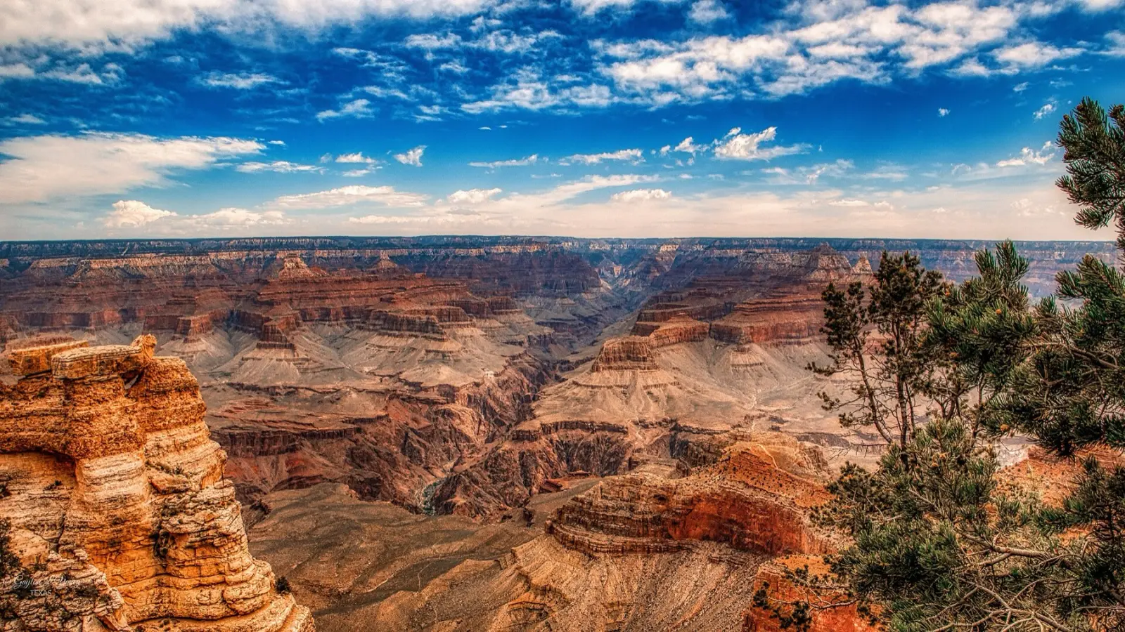 View into the Grand Canyon from Mather Point on the South Rim, layered red and tan rock under a blue sky with white clouds