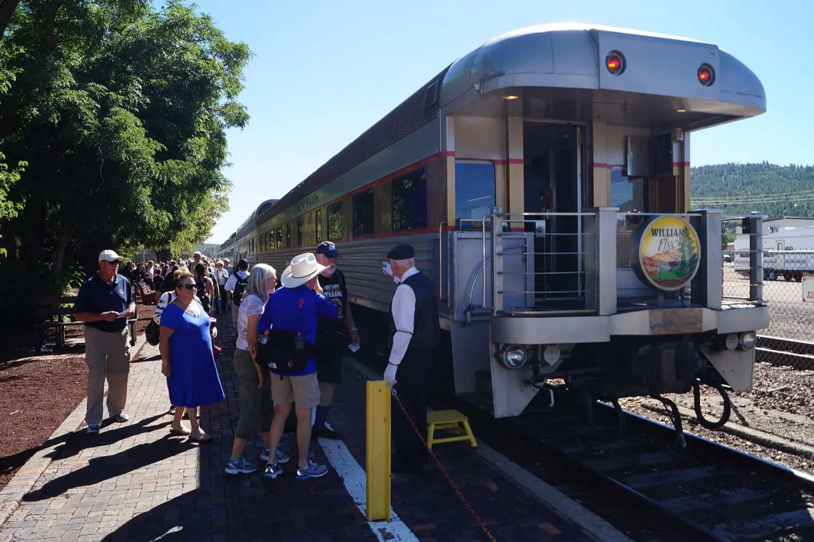 Passengers boarding a silver Grand Canyon Railway observation car with a Williams Flyer sign on the platform at the Williams depot