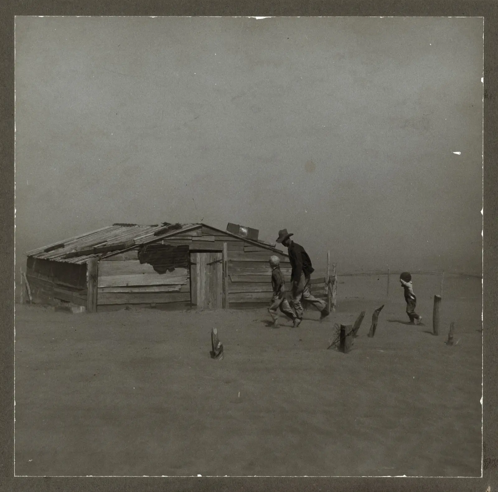 A farmer and his two sons walking toward a shed half buried by a dust storm in Cimarron County, Oklahoma, in 1936