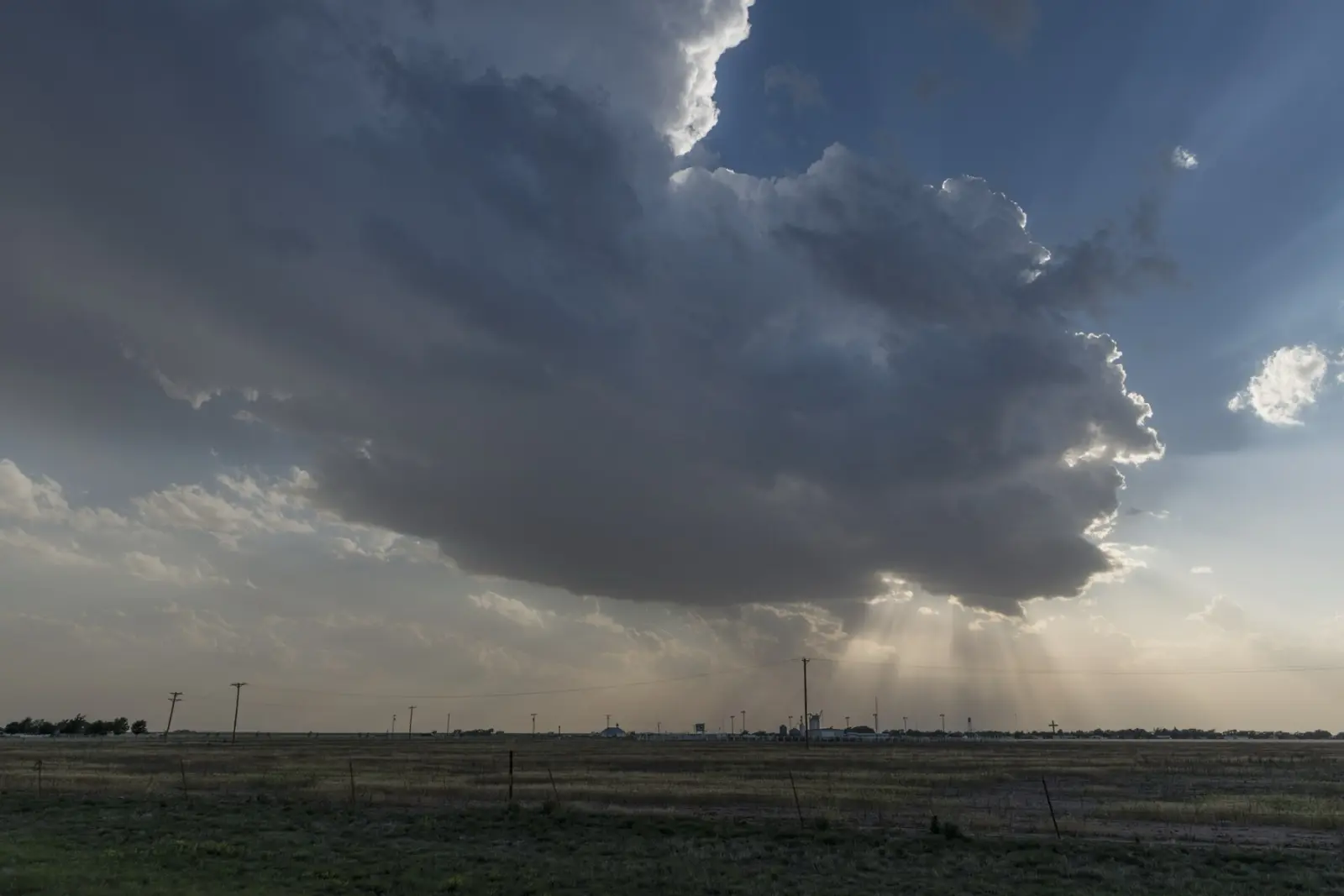 Huge storm cloud with sun rays breaking through over the flat Texas Panhandle at Groom, with power poles, grain elevators and the town on the horizon