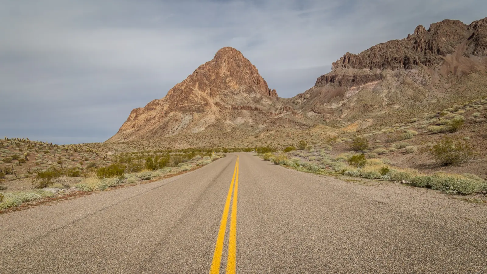 Empty two-lane road with a double yellow line running toward rocky desert peaks under a gray winter sky in Mohave County, Arizona
