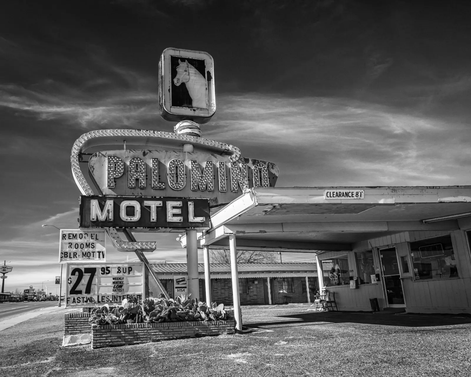 Black and white photo of the Palomino Motel sign with a horse head and a carport office on Route 66 in Tucumcari under a winter sky
