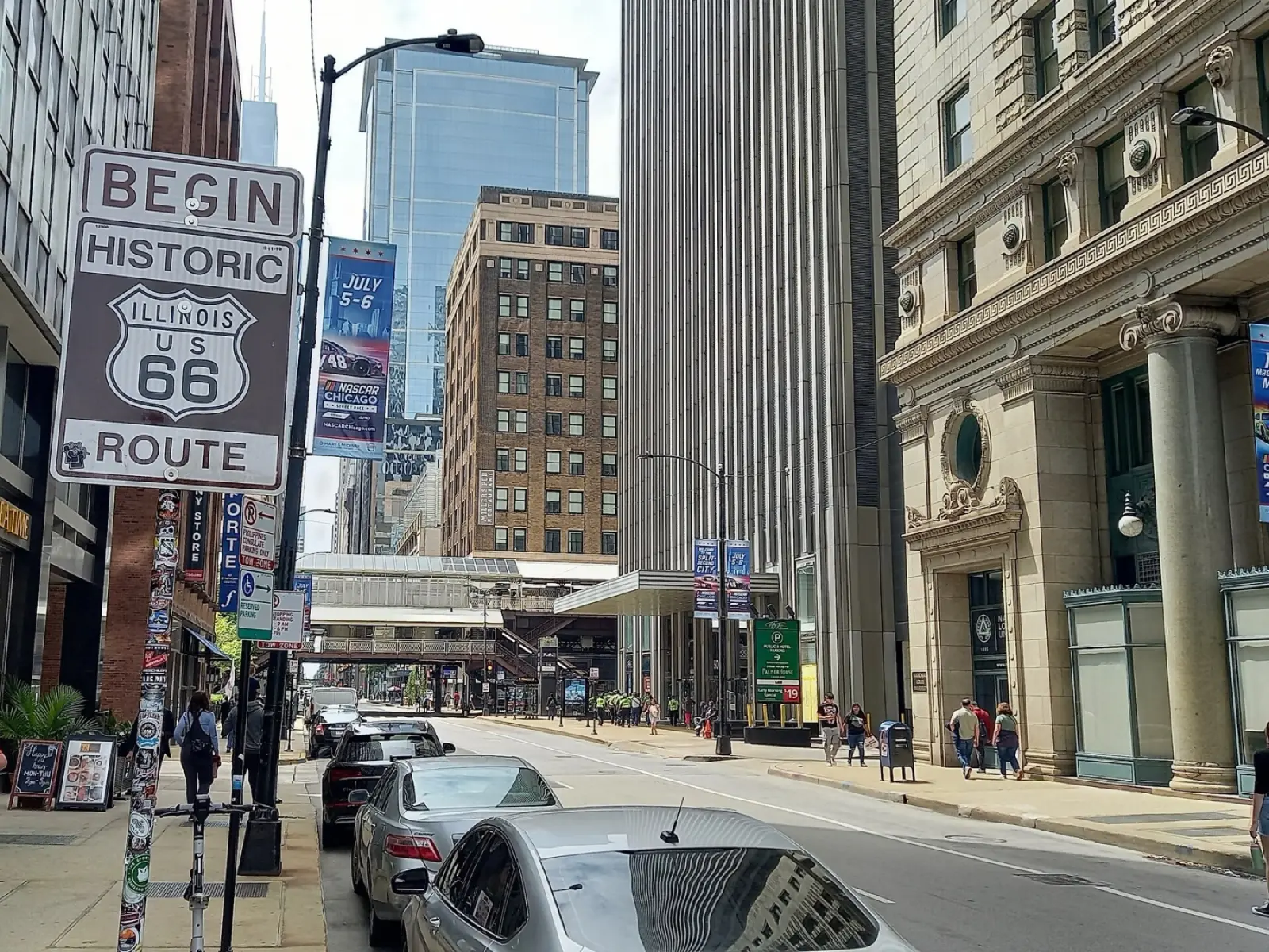 Brown Begin Historic Route 66 sign on a pole on Adams Street in downtown Chicago, with traffic and tall buildings behind it