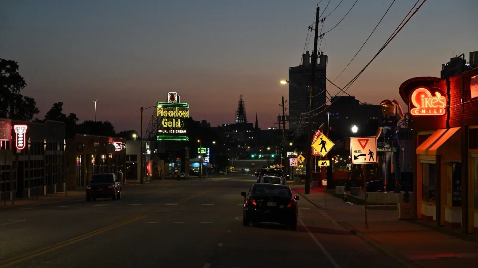 Route 66 on 11th Street in Tulsa at dusk, with the lit Meadow Gold neon sign and the Ike's Chili sign