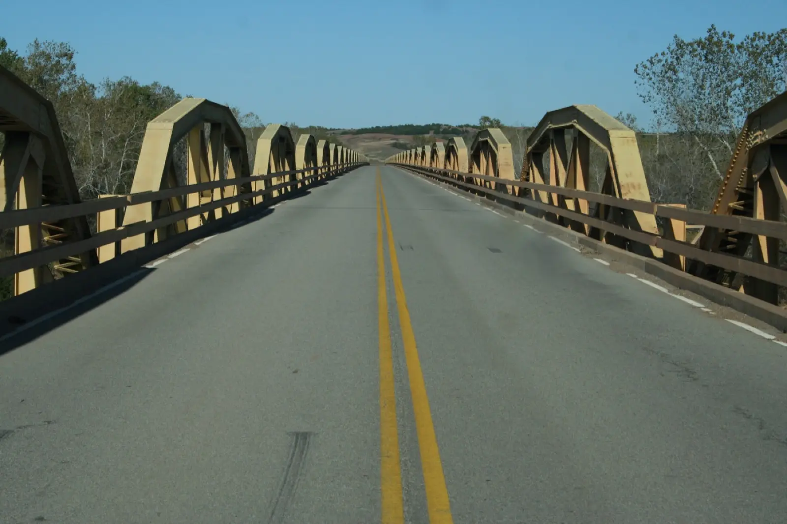 Two-lane road running between rows of yellow pony truss spans on the Bridgeport Pony Bridge over the Canadian River, Oklahoma