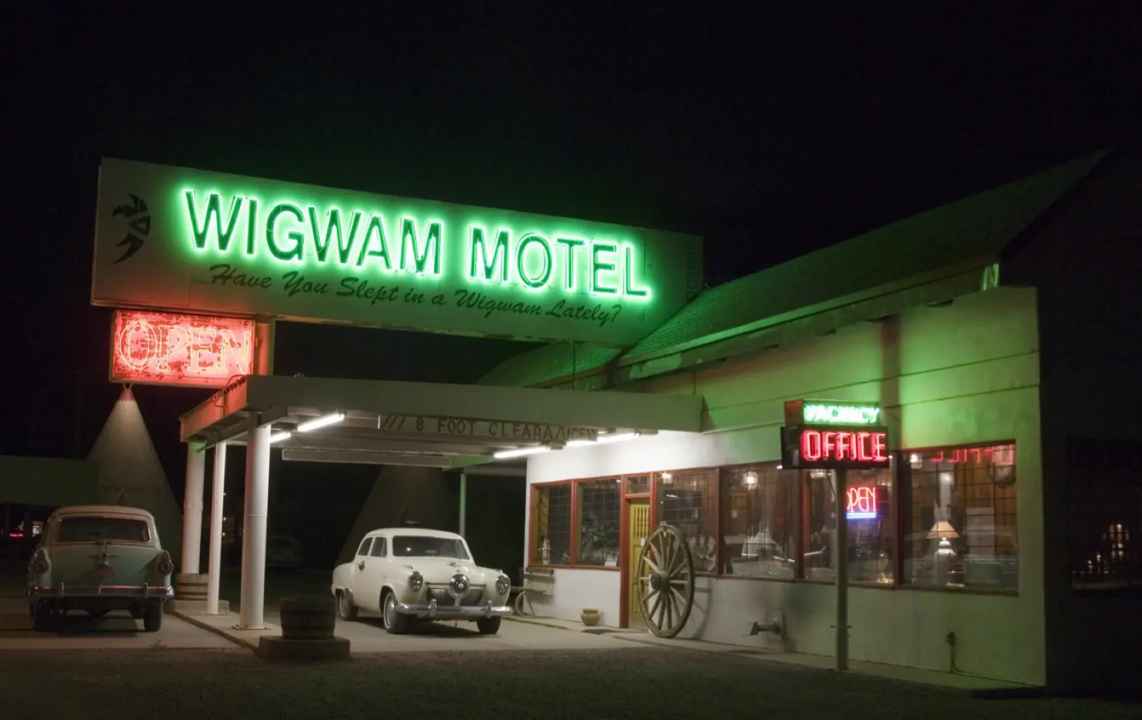 Green neon sign and office of the Wigwam Motel at night, with vintage cars and a concrete teepee, Holbrook, Arizona