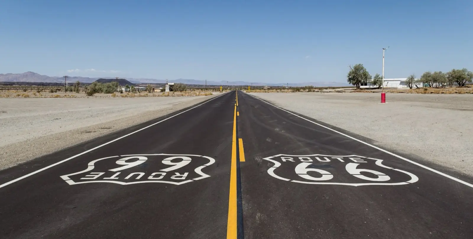 Two-lane Route 66 near Amboy, California, with Route 66 shields painted on the asphalt and desert mountains on the horizon