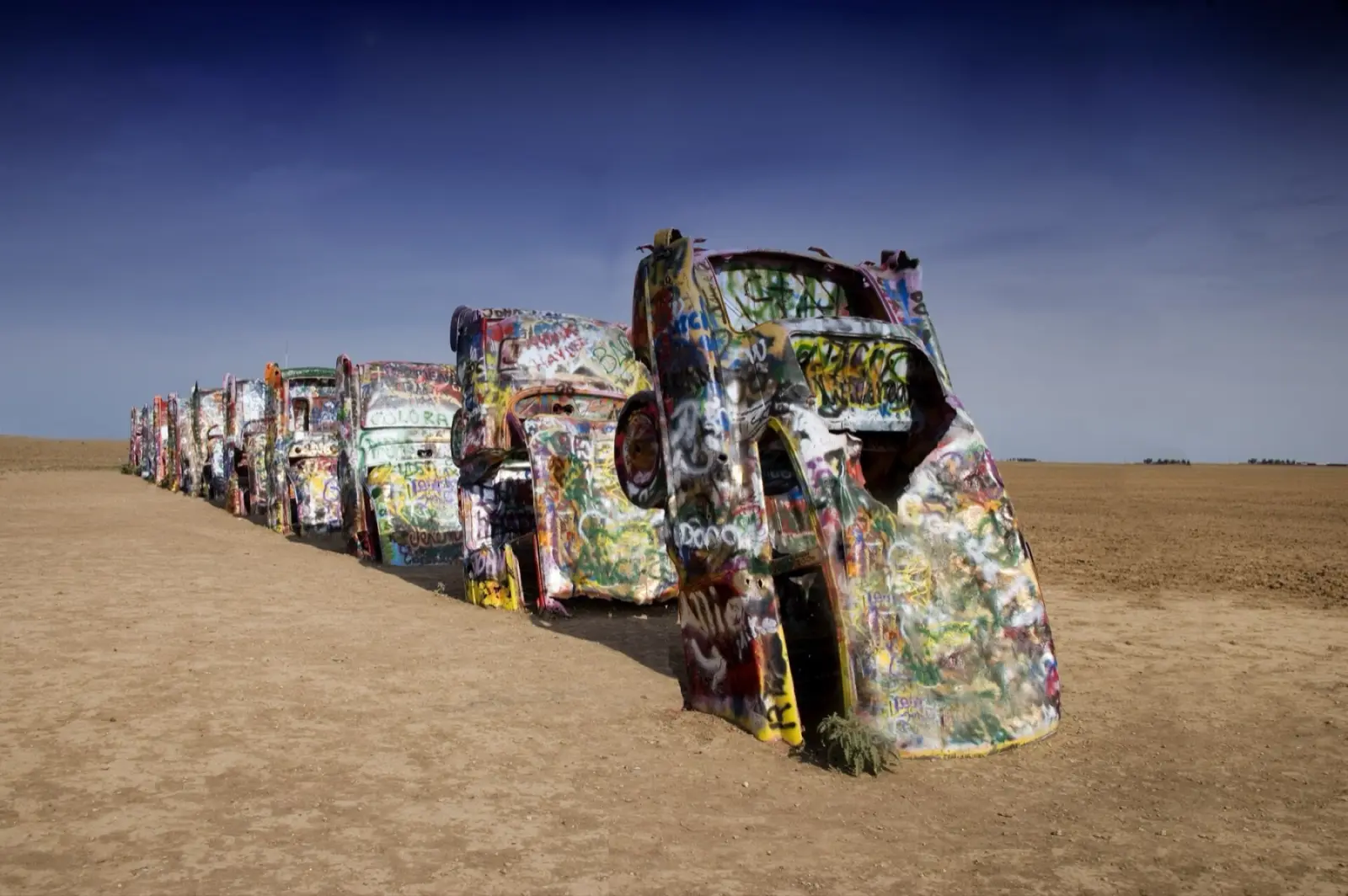 A row of graffiti-covered Cadillacs buried nose-down in a dirt field at Cadillac Ranch near Amarillo