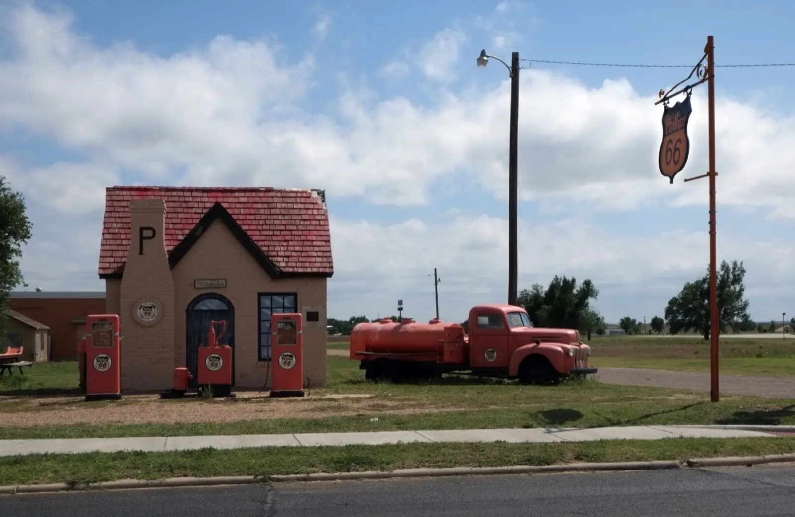 Restored brick Phillips 66 cottage station in McLean, Texas, with red tile roof, two vintage red pumps, an old red tanker truck and a Phillips 66 shield sign on a pole