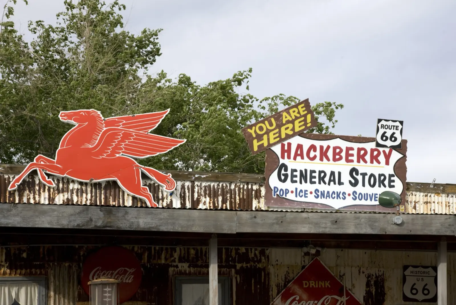 The roof of the Hackberry General Store in Arizona with a red Mobil Pegasus sign, a hand-painted store sign reading Pop, Ice, Snacks, Souvenirs, and Route 66 shields
